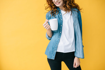 cropped view of cheerful curly woman holding cup and standing on orange
