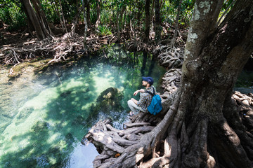 Man sitting on the roots of mangrove trees close to the pond in Krabi province, Thailand