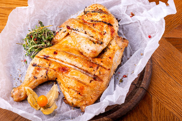 Grilled chicken Tabaka served with herbs on wooden background.
