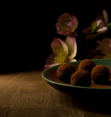 dark chocolate truffles in green plate on wooden, and pink flowers in background, golden light, copy space