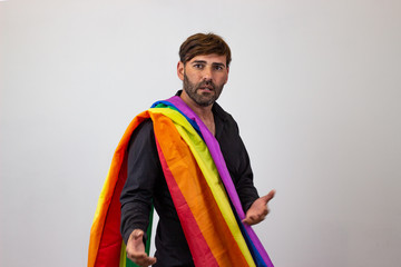 Portrait of handsome young man with gay pride movement LGBT Rainbow flag and brown hair looking annoyed, their back facing the camera and looking at the camera. Isolated on white background.