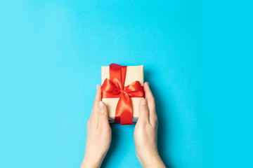 Top view of female hands holding a surprise gift box with a red bow