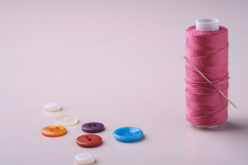 Angle view close up of pink thread coil with buttons and needle