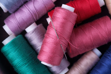Top view close up of scattered colorful cotton thread coils with needle
