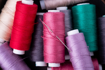 Top view close up of scattered colorful cotton thread coils with needle