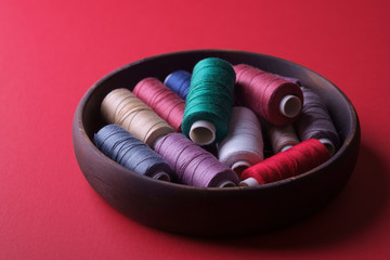 Angle view of scattered colorful cotton thread coils in wooden plate red background