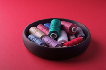 Angle view of scattered colorful cotton thread coils in wooden plate red background