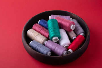 Angle view of scattered colorful cotton thread coils in wooden plate red background