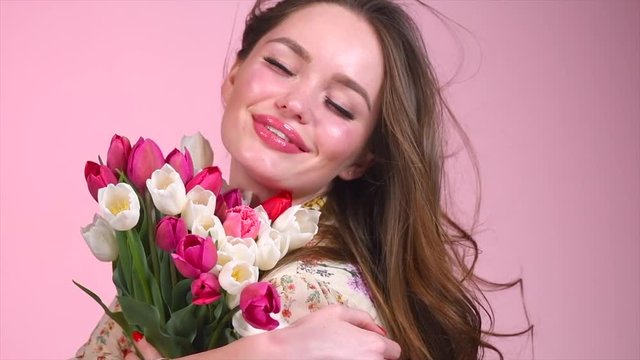 Beauty glamour girl with spring tulip flowers. Beautiful young woman with a bunch of colorful tulip flowers. Happy model posing with bouquet of tulips. Slow Motion 4K UHD video footage. 3840X2160