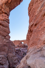 A sandstone arch frames another arch in the distance on a clear day with blue skies. Arches National Park, Utah. 