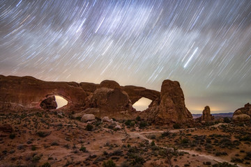 Star trails moving across the night sky over natural sandstone arches. The Windows in Arches...