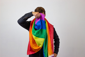 Portrait of handsome young man with gay pride movement LGBT Rainbow flag and brown hair pointing at an object to the side, looking at the camera. Isolated on white background.