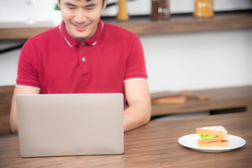 The blur business man with casual  red t-shirt messaging on mobile phone, drinking coffee and eating sandwich, Young man working on labtop or computer  in the kitchen room, loft style