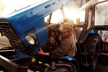 Farmer mechanic repairing blue tractor engine. Repair agricultural technology at sunset.