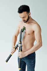 shirtless man in jeans cutting plant on chest with big scissors isolated on grey