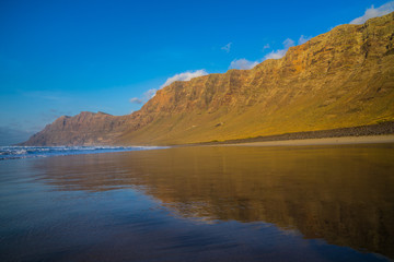 Spain, Lanzarote, Impressive famara massif mountains reflecting in wet sand of famara beach at sunset