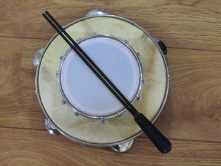 Fototapeta premium Two Brazilian percussion musical instruments: pandeiro (tambourine) and tamborim with drumstick on a wooden surface. The instruments are widely used to accompany samba, a popular Brazilian rhythm.