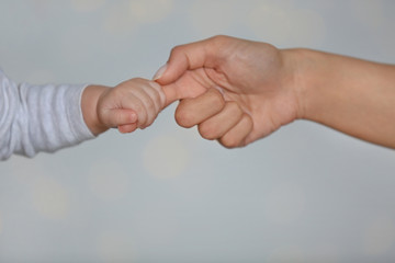 Obraz premium Little baby holding mother's finger on light background, closeup