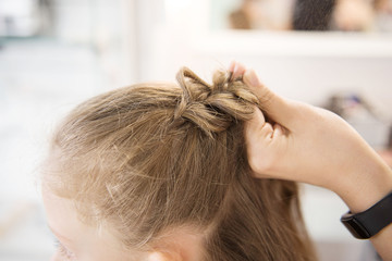 Naklejka premium Hairdresser weaving plaits in beauty salon. Hairdressing services. Сreating hairstyle. Hair styling process. Children's hairdressing salon.
