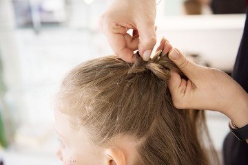 Fototapeta premium Hairdresser weaving plaits in beauty salon. Hairdressing services. Сreating hairstyle. Hair styling process. Children's hairdressing salon.
