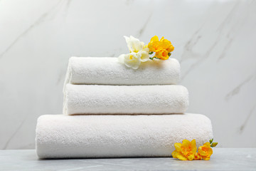 Stack of fresh towels with flowers on grey table against light background