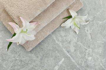 Stack of fresh towels with flowers on grey table, top view. Space for text