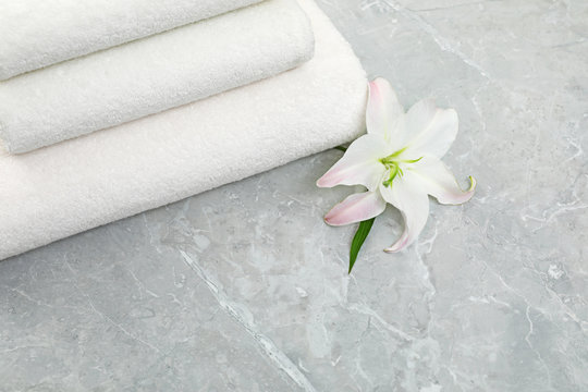 Stack of fresh towels with flower on grey table, above view. Space for text