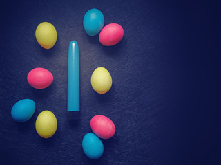 Blue vibrator (sex toy) and colorful eggs are on a dark textured background. Image suitable for advertising sex shop.
