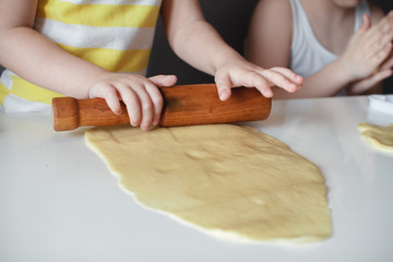 Little cute girl making shortbread. Rolls out the dough with a rolling pin on a white table. The preparation of the dessert. close-up