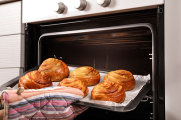Woman taking freshly baked buns out of oven, closeup