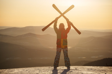 Fototapeta premium A skier holds skis in his hands against the sunset sky.