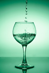 Wine glass with flowing water (white wine) on a background of green gradient