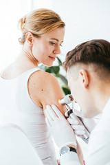 Fototapeta premium dermatologist in latex gloves holding dermatoscope while examining beautiful patient with skin disease