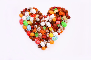 nuts, dried fruits, sweets laid out in the shape of a heart on a white background healthy and unhealthy food concept