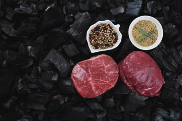 Pair of raw marbled beefsteaks with condiments on charcoal background, flatlay with copy space, horizontal shot