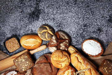 Assortment of baked bread and bread rolls on rustic grey bakery table background