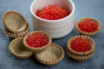 Tartlets with red caviar over blue stone background, close-up, horizontal shot