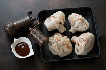 Cast-iron serving tray with georgian traditional meat dumplings khinkali over dark brown metal...