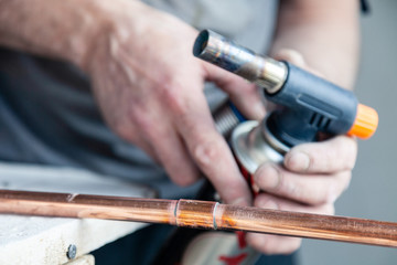 Closeup professional master plumber holding flux paste for soldering and brazing seams of copper pipe gas burner. Concept breaking, installation and changing in apartment building pipeline, leakage