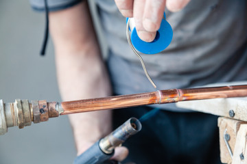 Closeup professional master plumber holding flux paste for soldering and brazing seams of copper pipe gas burner. Concept installation and repair of an apartment building pipeline, leakage