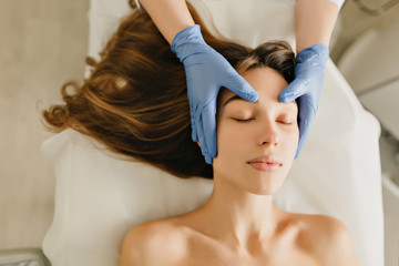 Fototapeta na wymiar View from above joyful woman with long brunette hair relaxing from massage on head from professional cosmetologist. Time for beauty, healthcare, rejuvenation