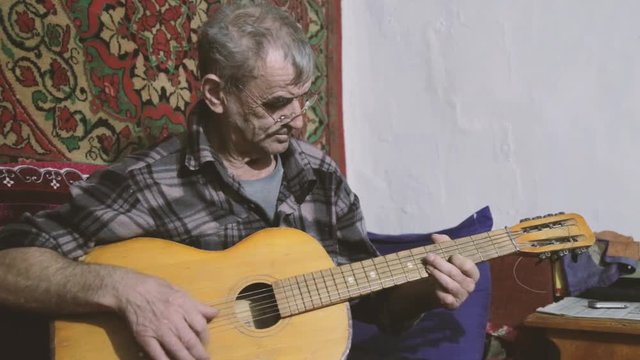 An elderly man plays the guitar,poor grandpa playing the guitar