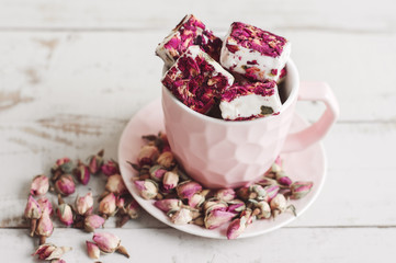Nougat with edible flower petals in a pink coffee cup and dried rose buds. Lebanese sweets. Turkish delight
