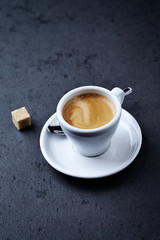 Cup of coffee and a brown sugar cube on dark stone background. Copy space