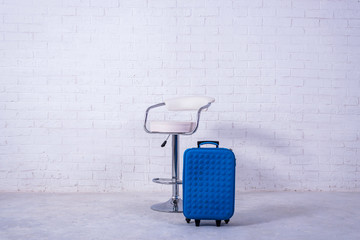 Blue suitcase and high chair near the white brick wall. Space for text