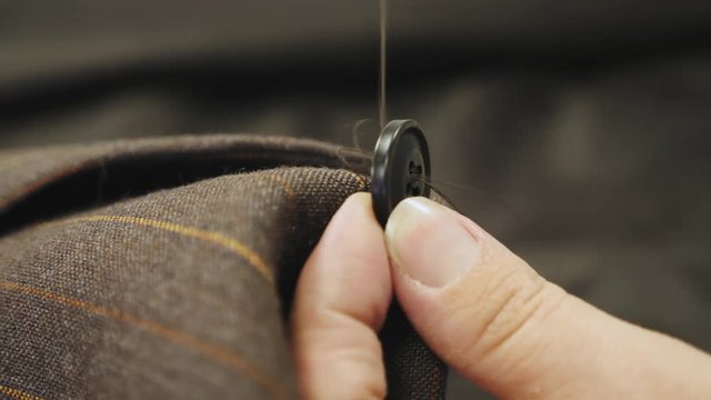 Sewing a button onto a brown jacket tailored suit
