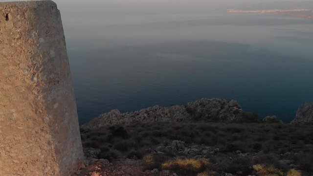 Aerial sunrise part rotation around pirate watchtower, Torre Vig&iacute;a De Cerro Gordo, Andalusia, Southern Spain. Revealing rugged coastal cliff and sea views towards Nerja and Torrox in the distant.