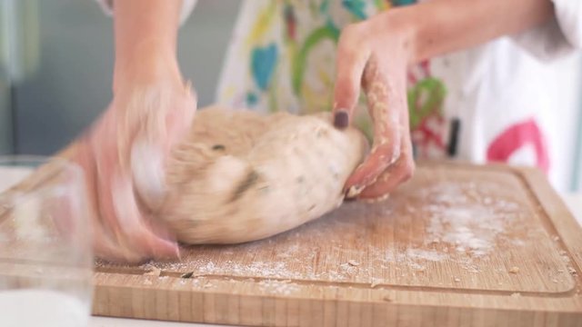 Chef kneading homemade bread dough on a wooden board, in a light filled kitchen, continued.