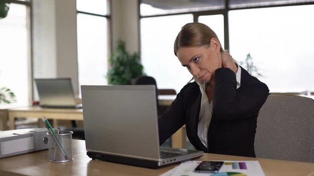 Employee suffering neck pain while working on laptop, stressful day in office