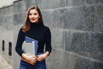 Beautiful girl standing near gray wall. Lady with a tablet. Woman on the street